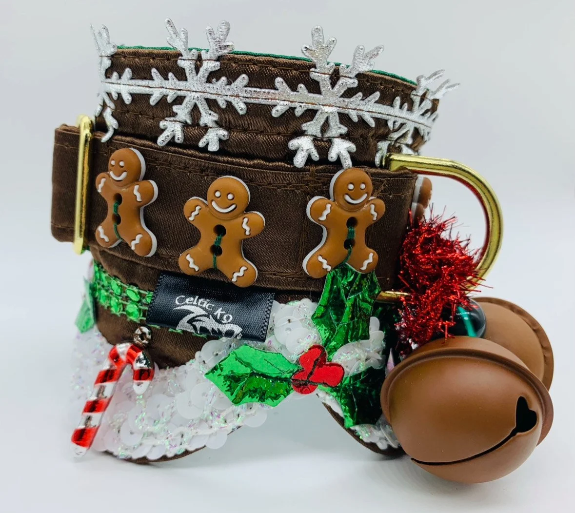 A collection of Christmas decorations and ornaments arranged inside a brown pet collar. The decorations include gingerbread man charms, a snowflake embellishment, a candy cane, holly leaves, red tinsel, and jingle bells.