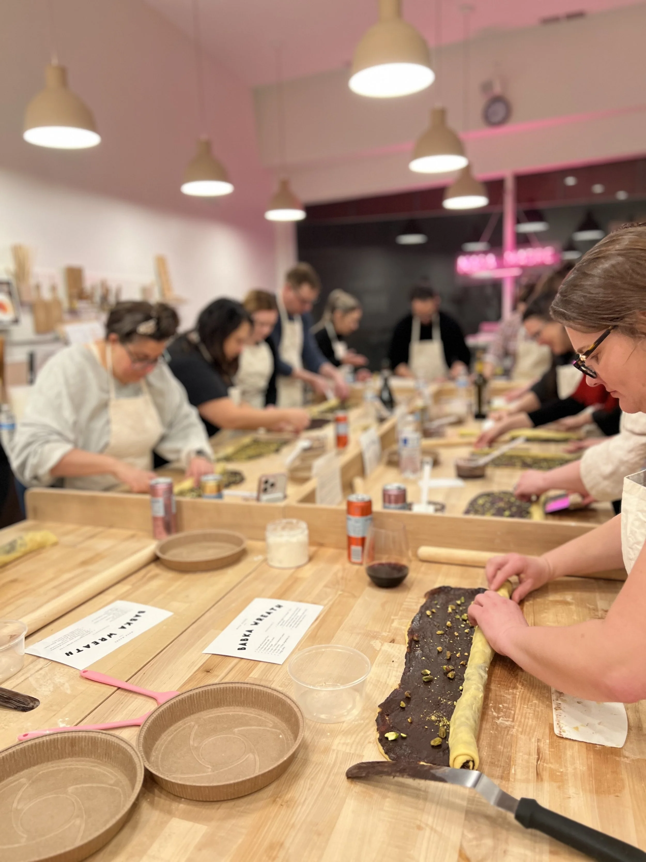 People participating in a baking class, rolling dough with pistachios on a wooden table.