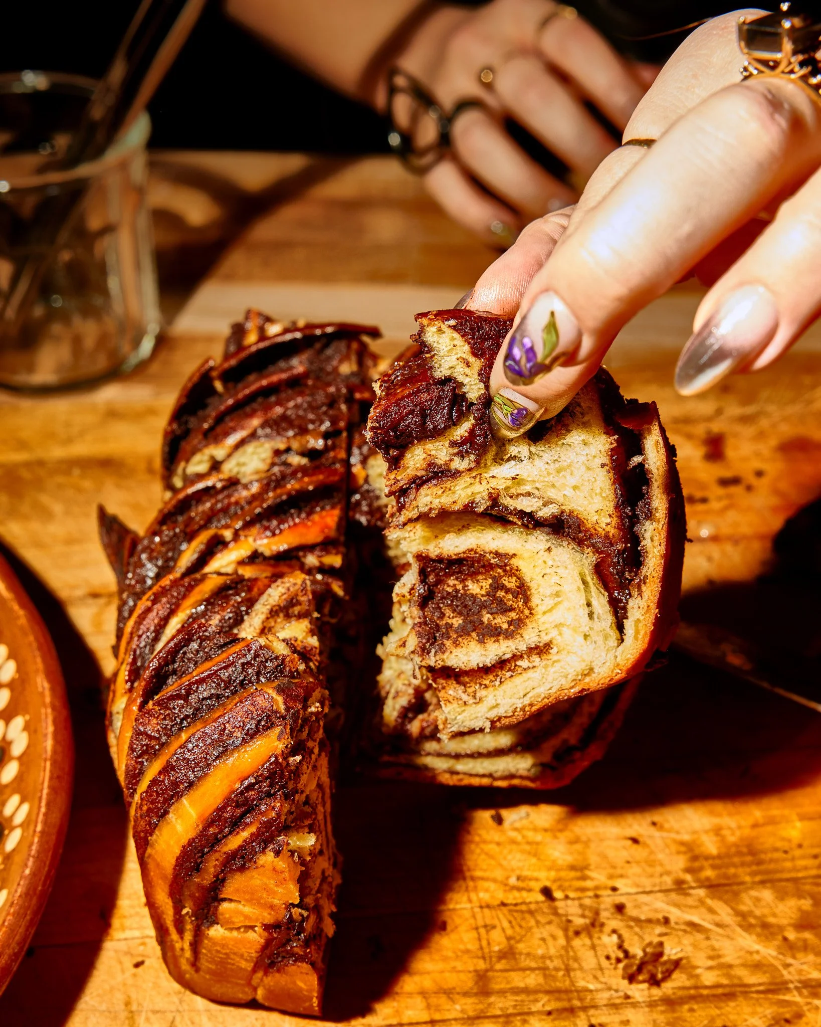 Person tearing into a cinnamon roll with chocolate and caramel topping, revealing its swirl shape and soft interior.
