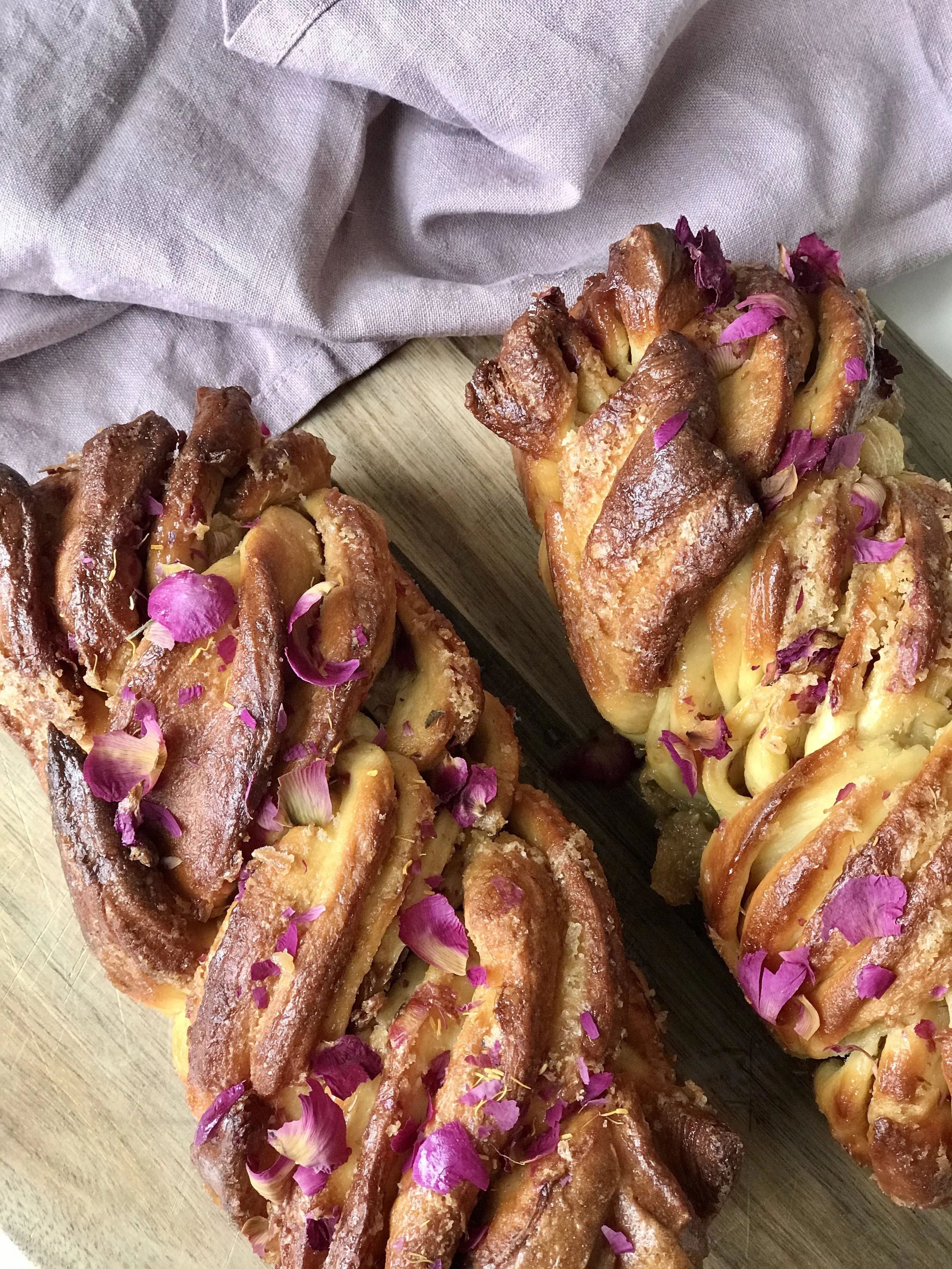 Sweet bread filled with cheese, topped with pink flower petals, on a wooden cutting board with a light cloth in the background.