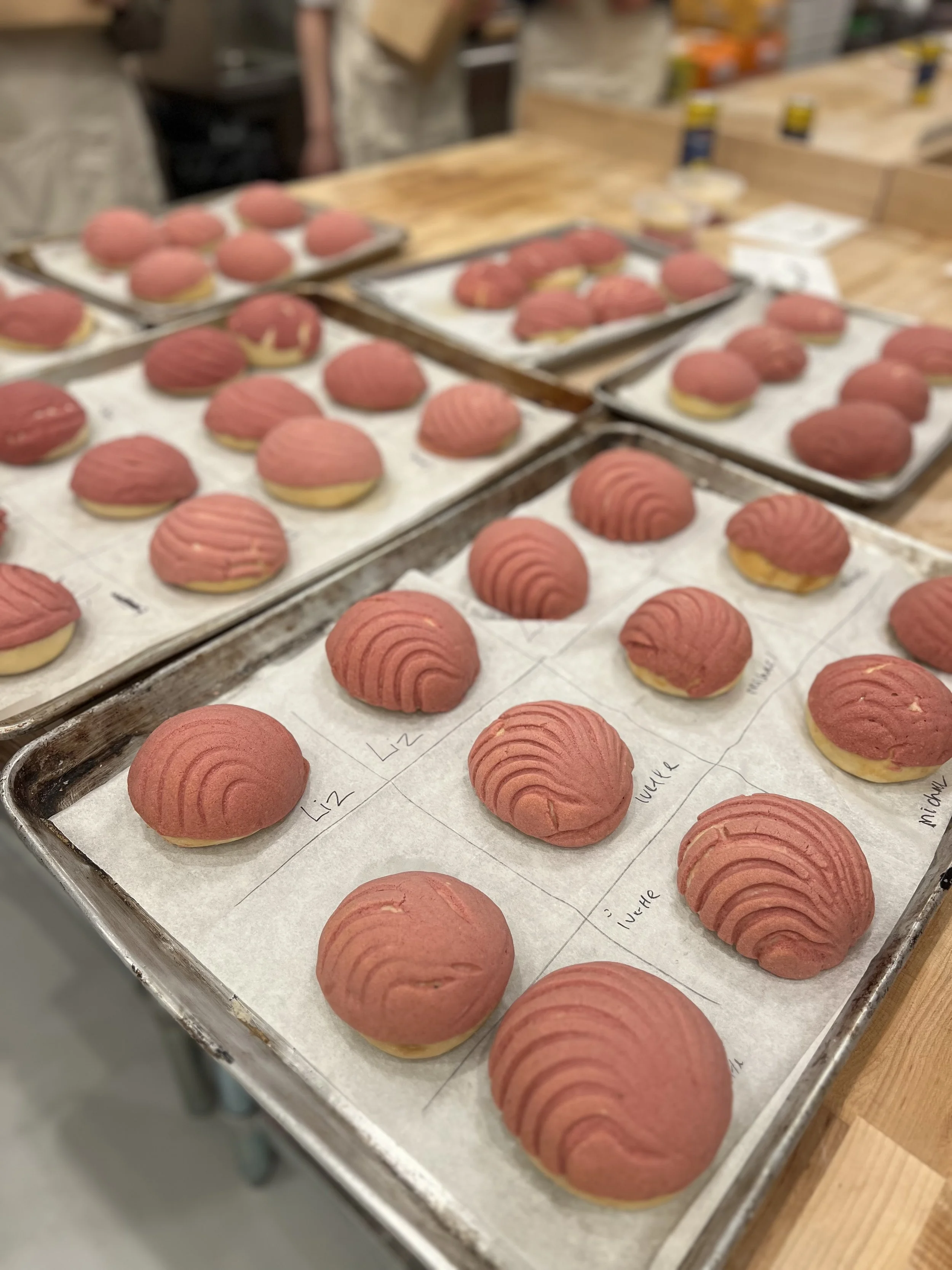 Batches of pink and yellow cookies with ridged tops on baking trays, ready to be baked or cooled.