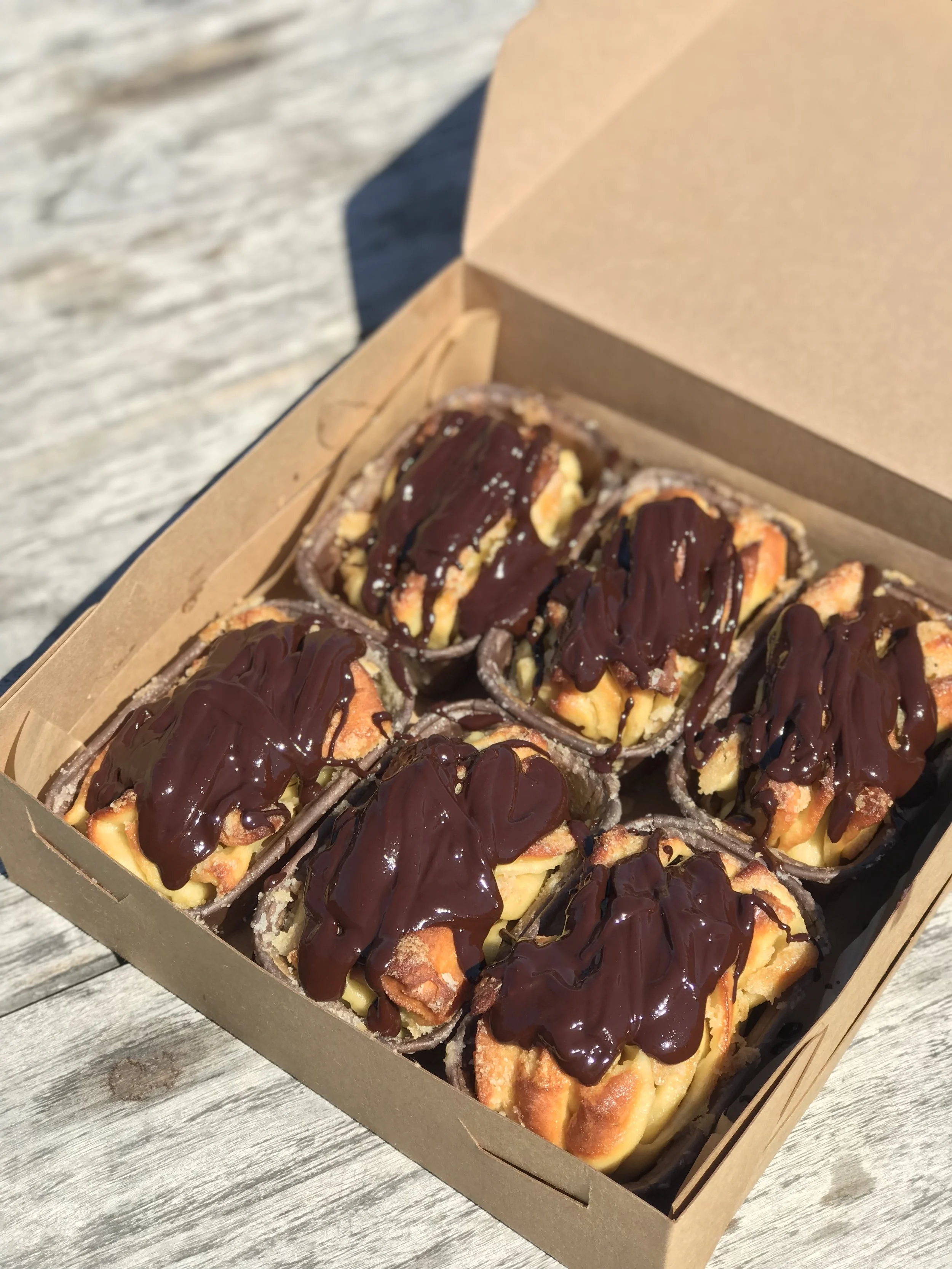 Six slices of banana chocolate croissant bread pudding topped with chocolate sauce in a cardboard takeout box.