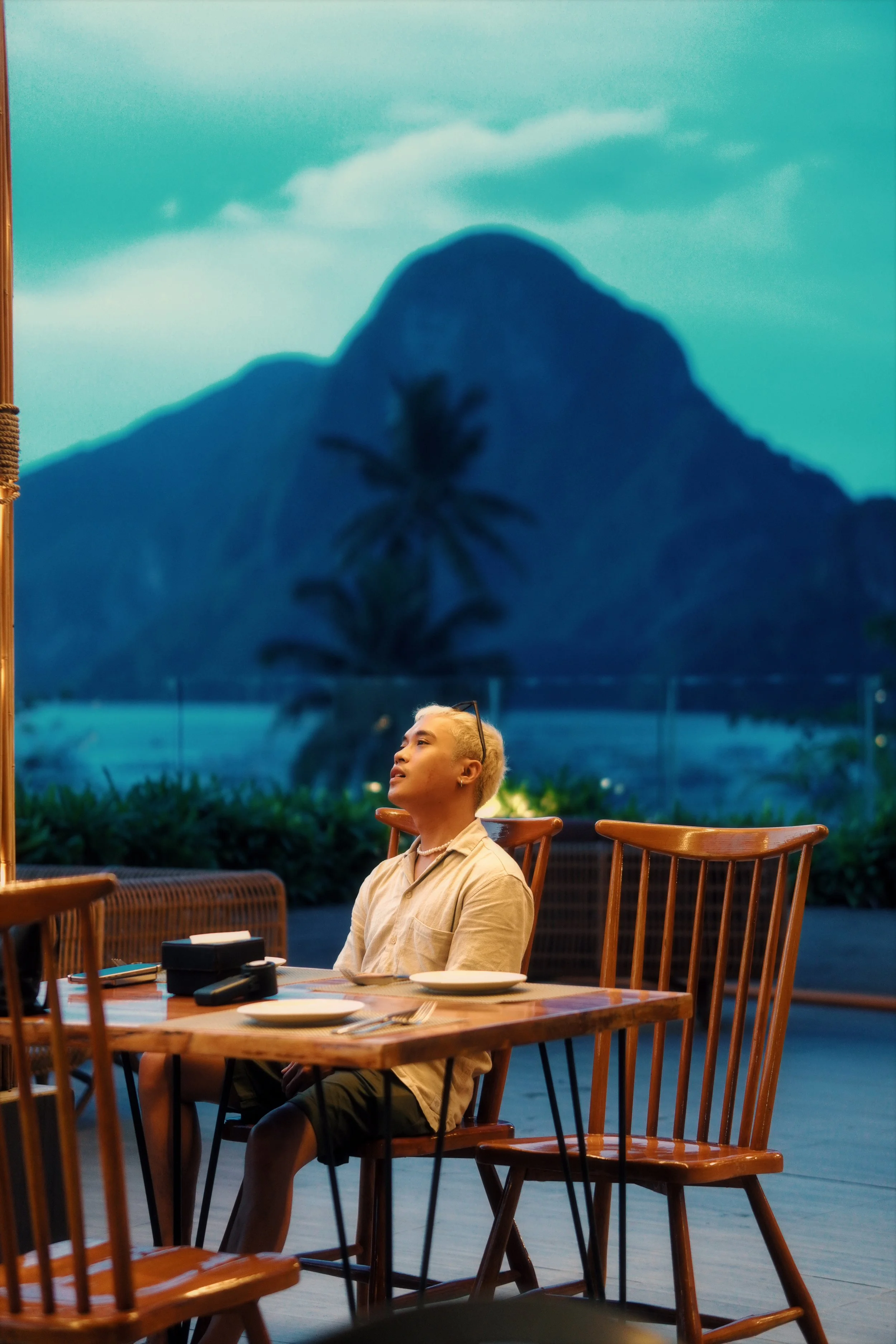 Person sitting at a wooden table in a restaurant with mountain and palm tree view outside
