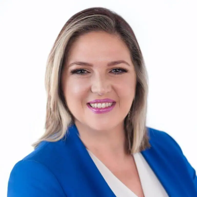 Portrait of a woman with blonde hair, wearing a blue blazer and white top, smiling against a plain white background.