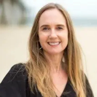 A woman with long blonde hair smiling outdoors near a body of water.
