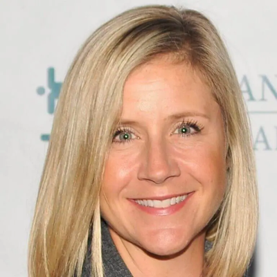 A smiling woman with blonde hair and blue eyes posing in front of a white background with blue text.