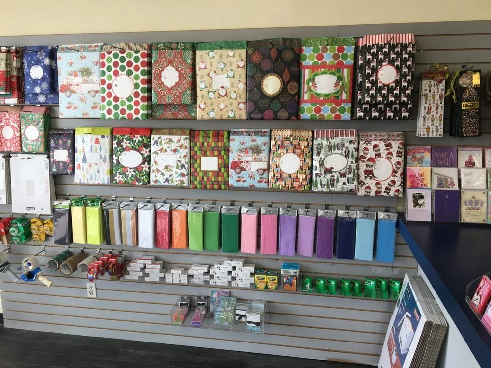 Display of Christmas-themed gift bags, wrapping paper, and related decorations on retail slatwall.