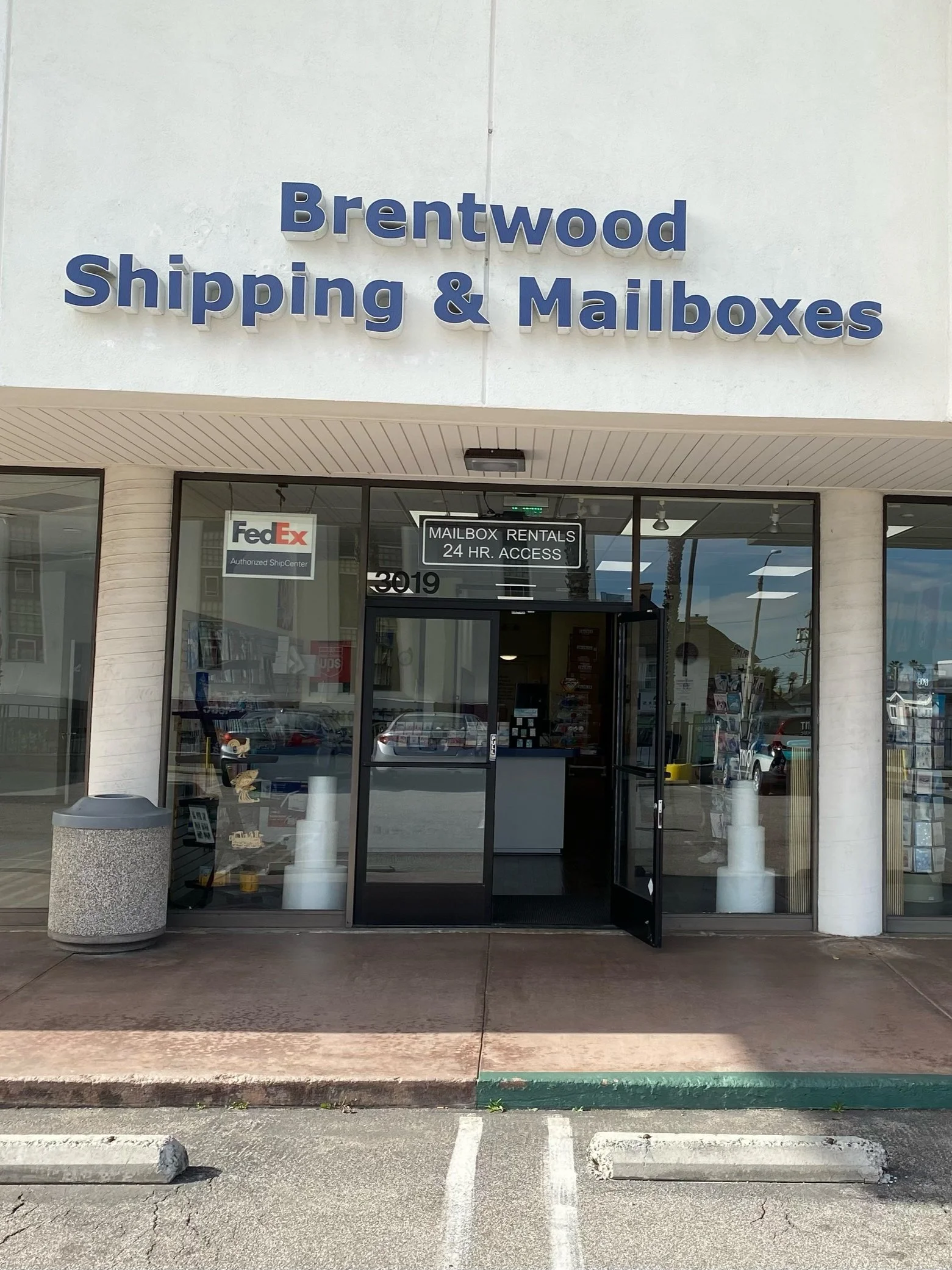 Exterior view of a shipping and mailbox store with large blue sign, glass doors, and windows, and a parking lot in front.