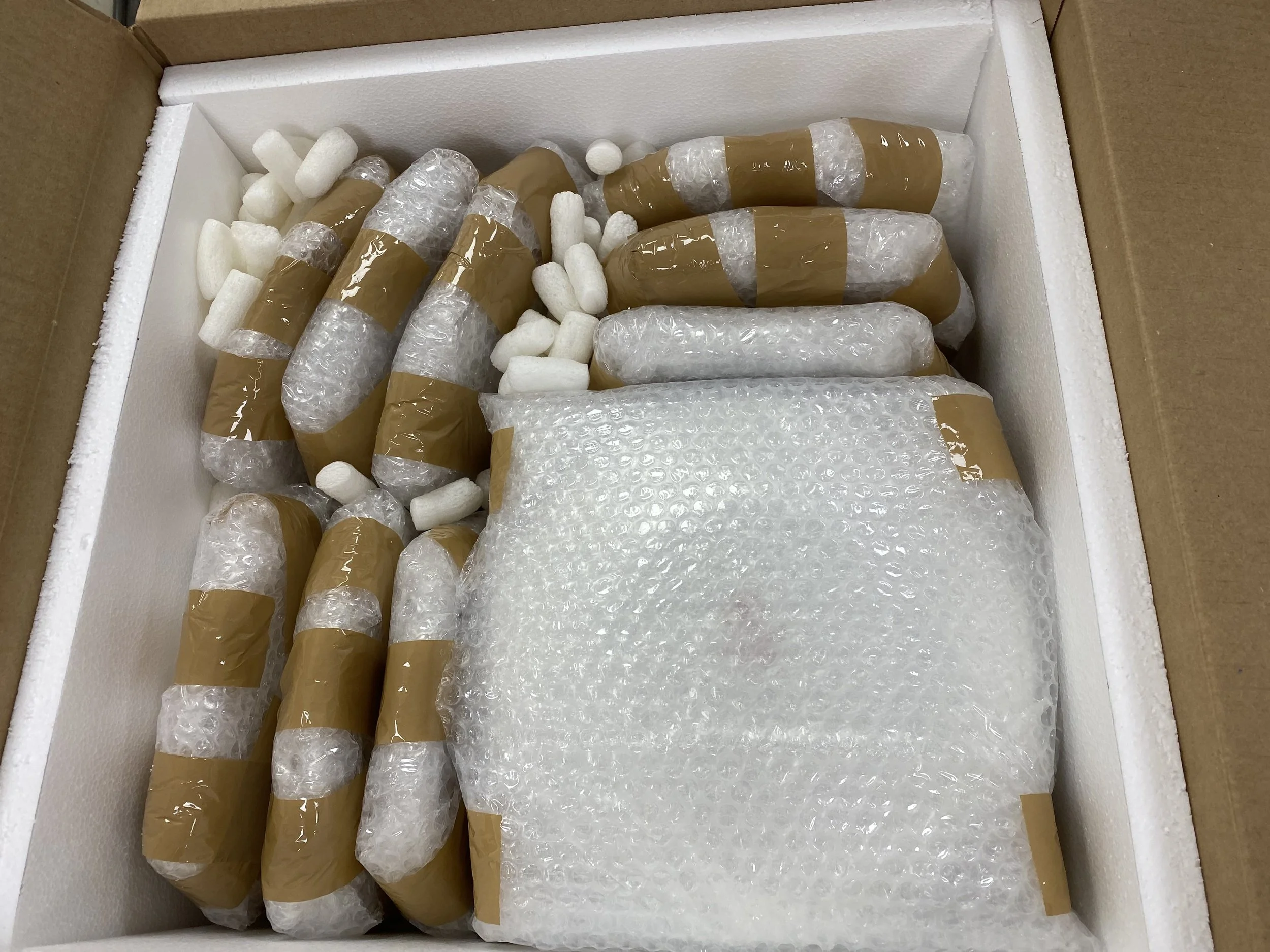 A box filled with several wrapped brown bottles and white packing peanuts for shipping.