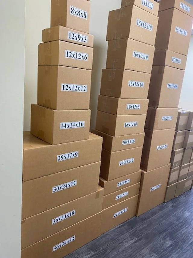 Stacks of cardboard boxes with size labels in a storage room or warehouse.