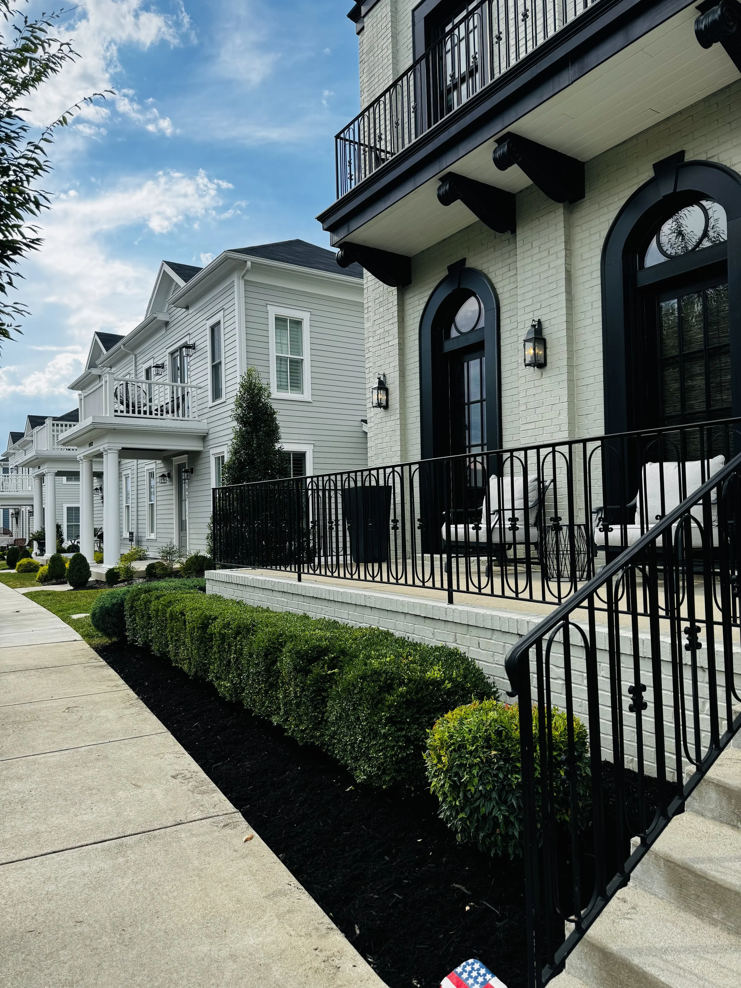 Modern row of white houses with black balconies and lush green bushes.