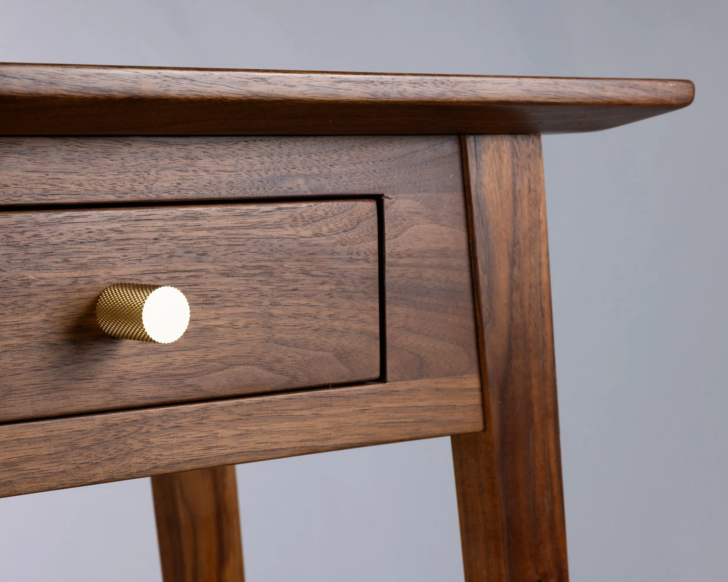 Close-up of a wooden nightstand with a single drawer, featuring a gold textured knob.