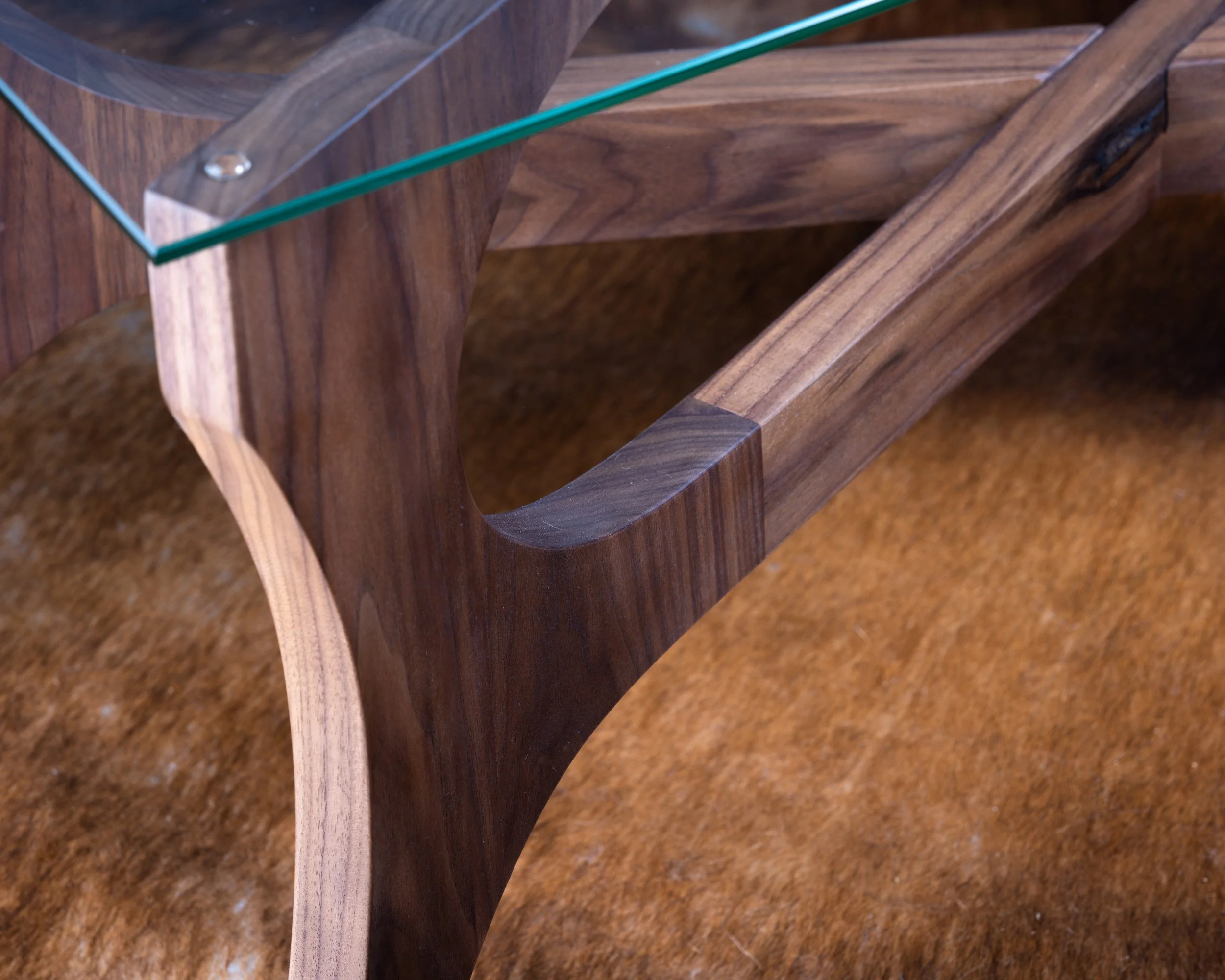 Close-up view of a wooden table with a glass top, showcasing the curved and polished wooden legs and frame.