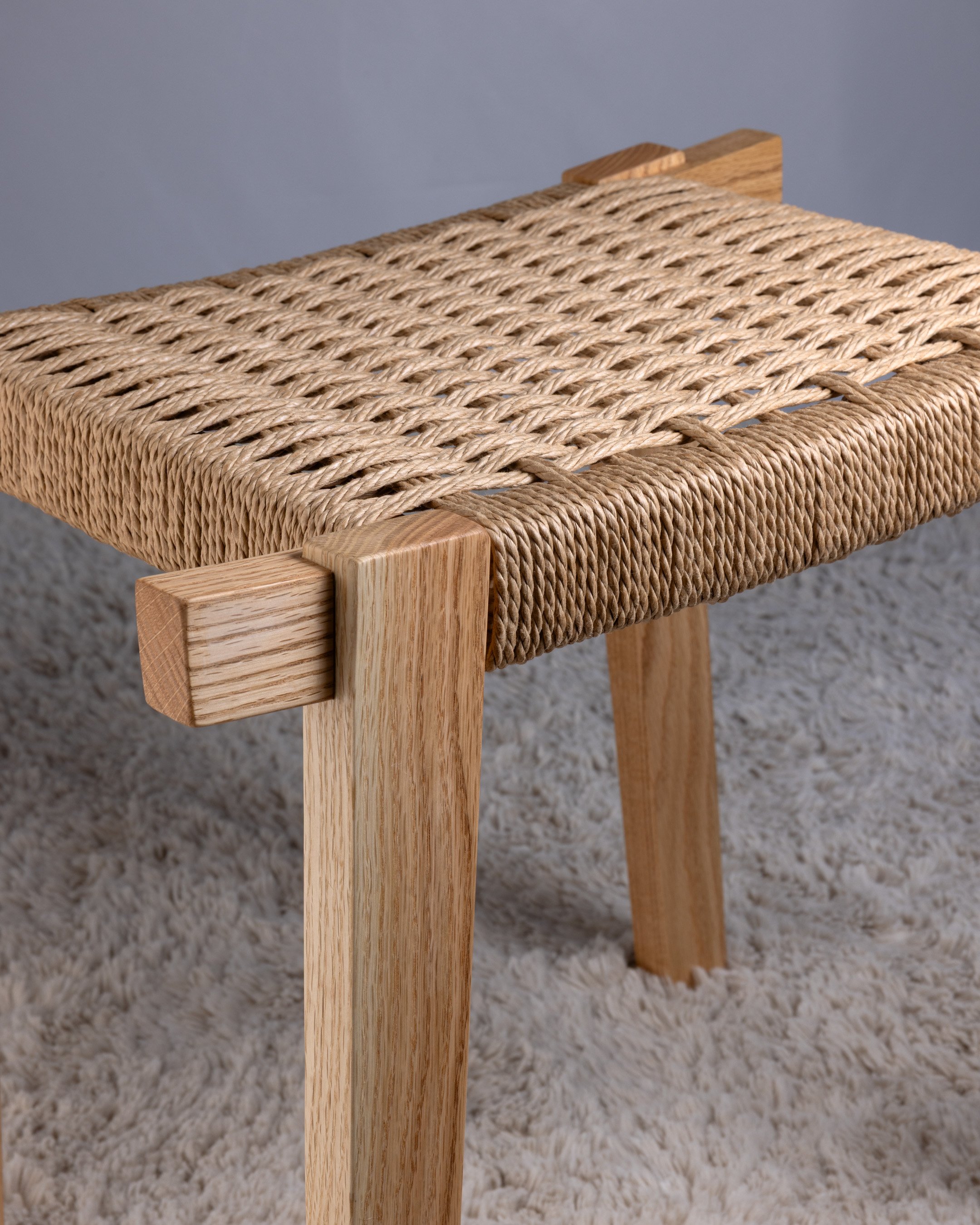 Close-up of a wooden stool with woven natural fiber seat.