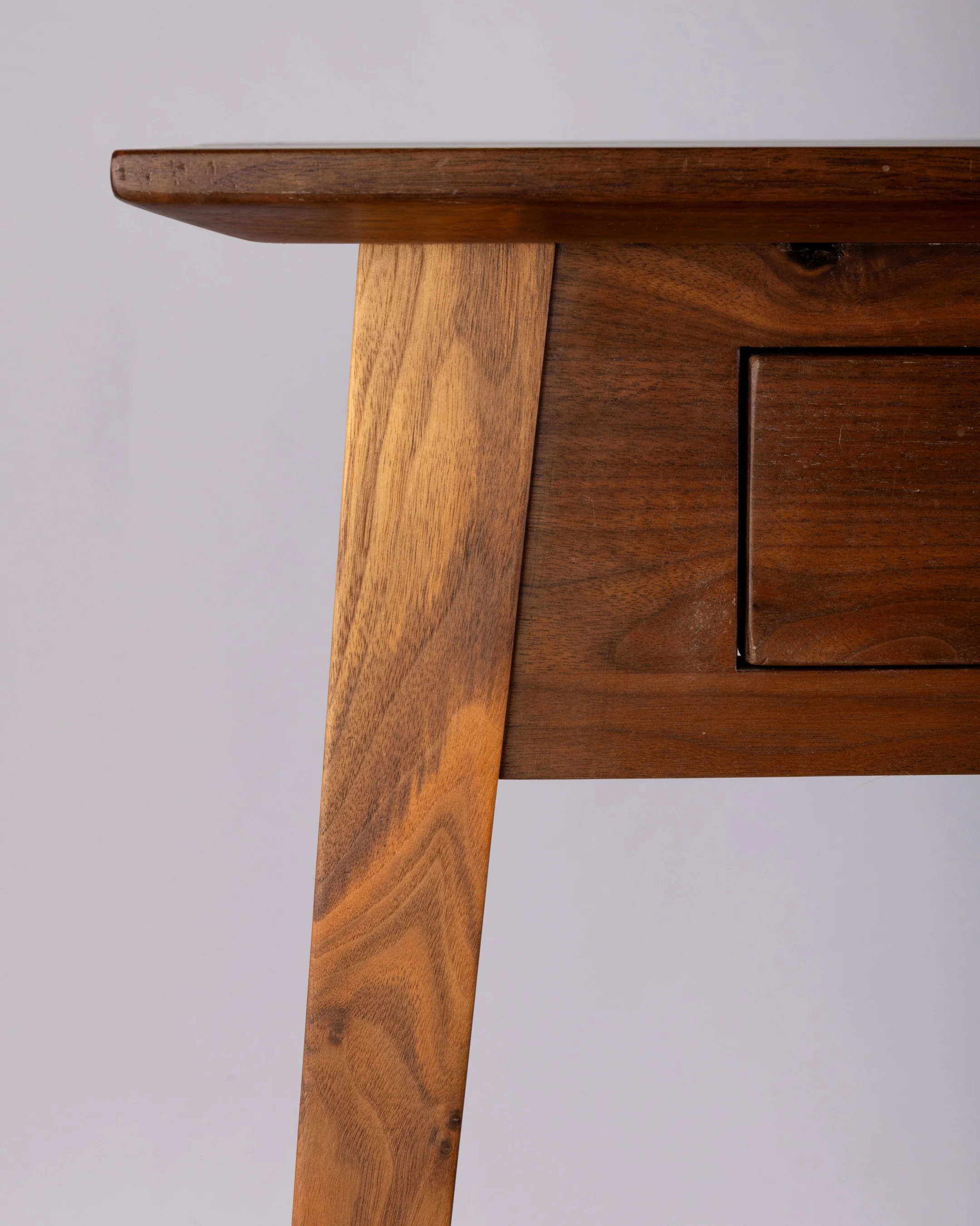 Close-up of a wooden table corner showing the edge and leg, with a wood drawer.