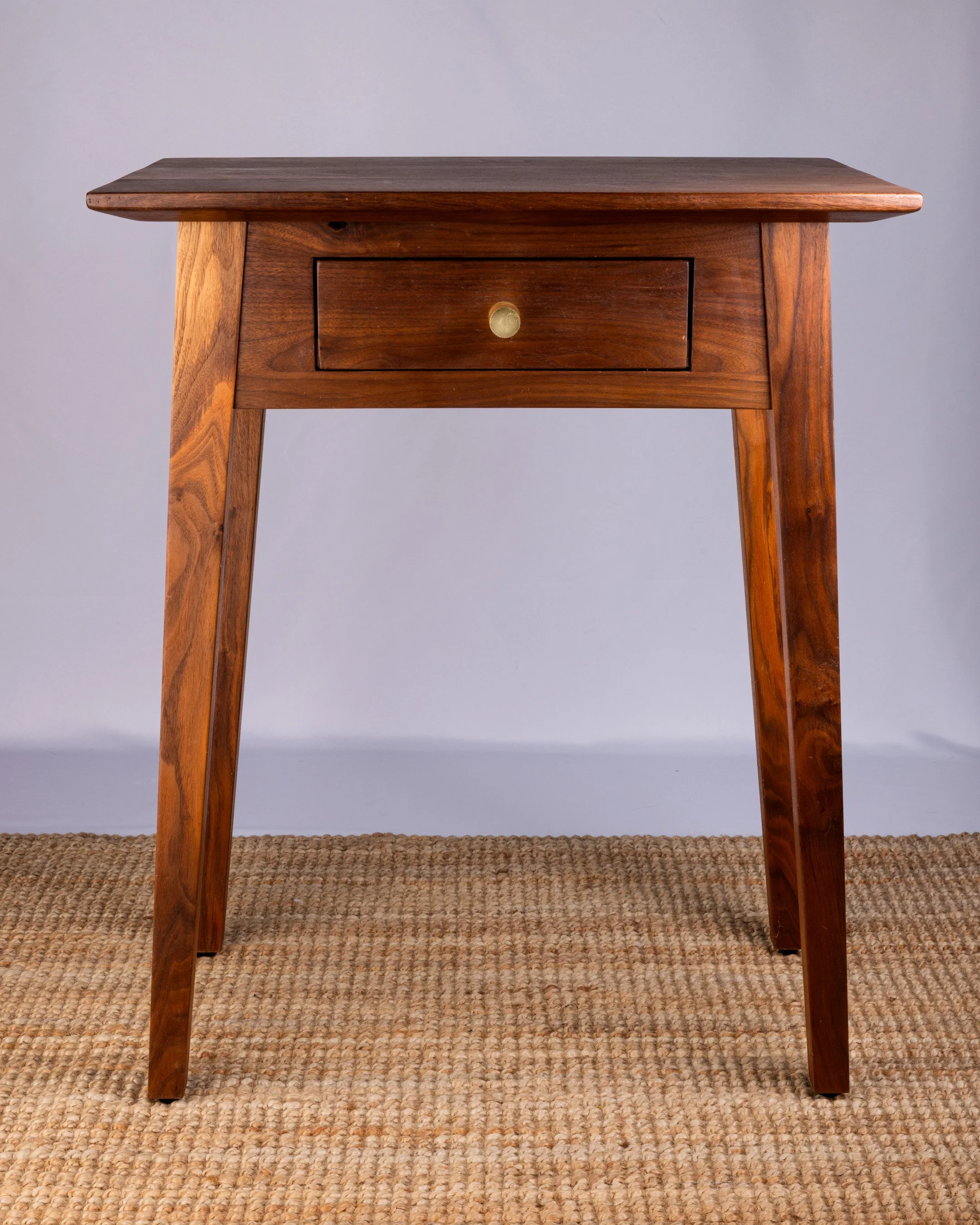 A wooden side table with a single drawer and a round brass knob.