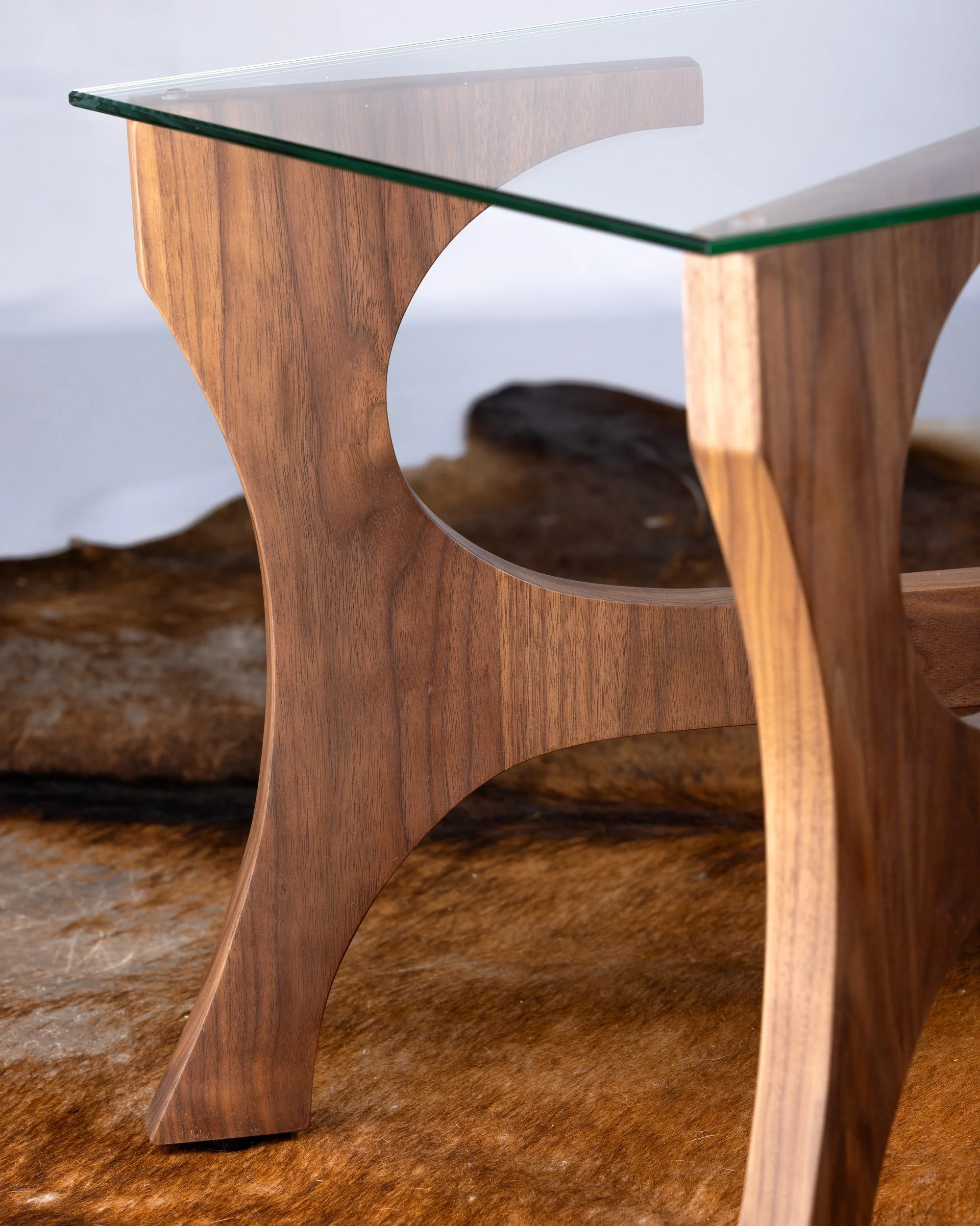 Close-up of a wooden table with a glass top, featuring curved legs and a circular cutout in the middle.