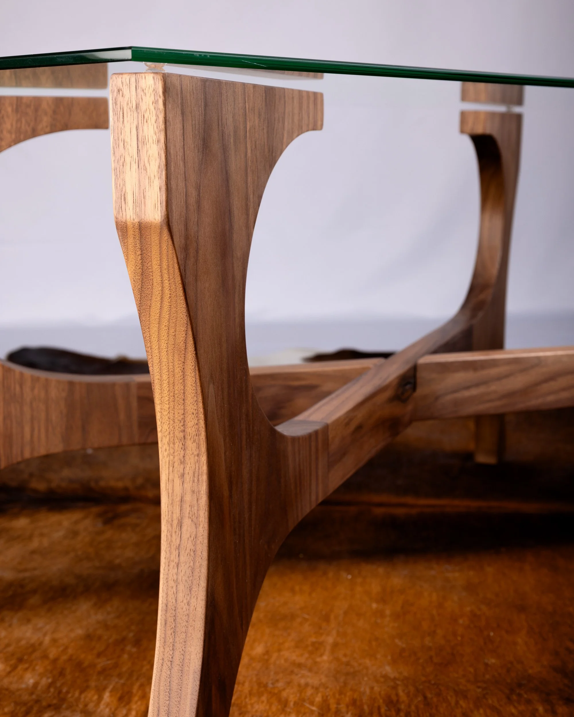 Close-up of a modern wooden and glass coffee table with curved wooden legs and a glass top.