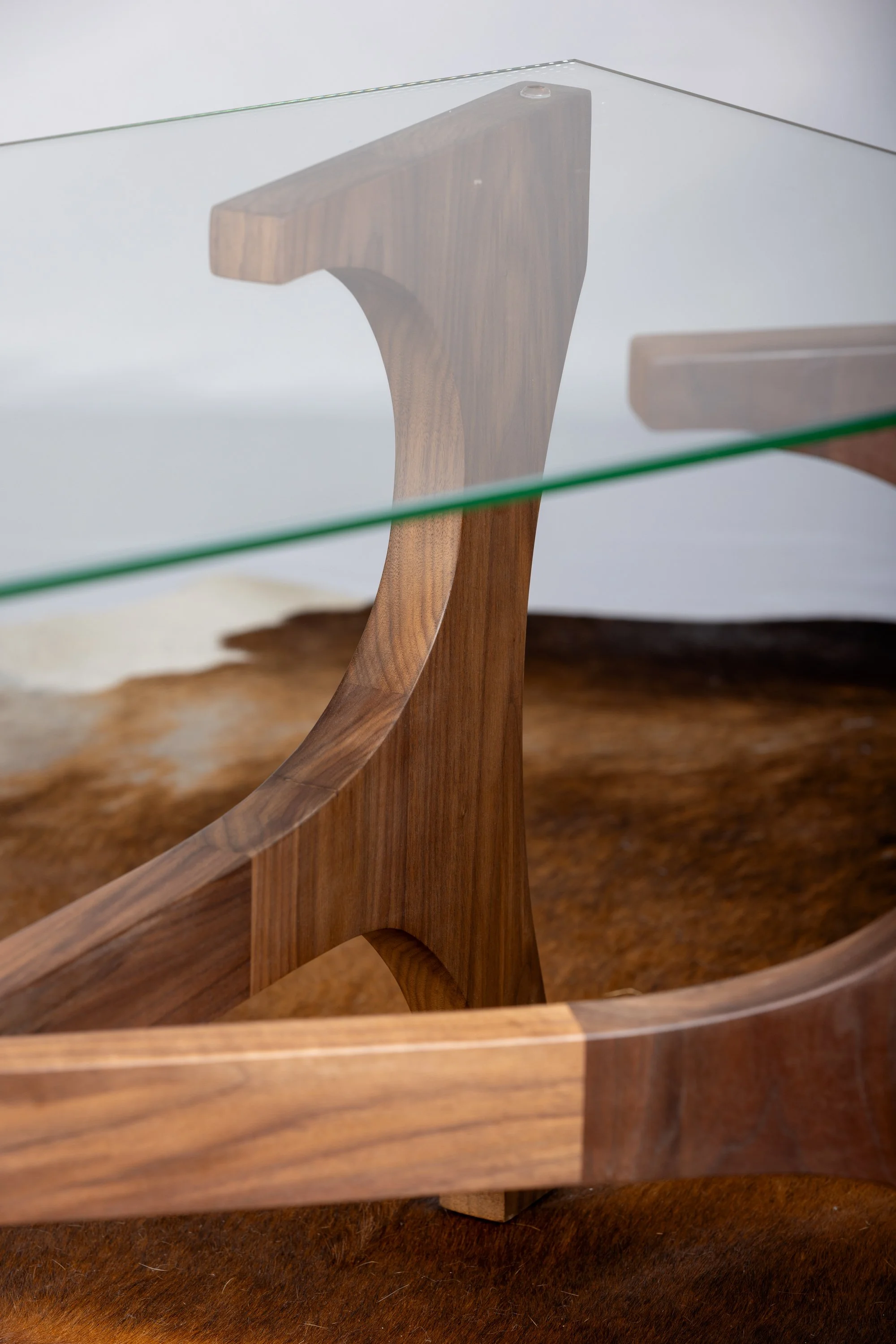 Close-up of a wooden table with a curved design, supported by a central wooden leg, with a glass top.