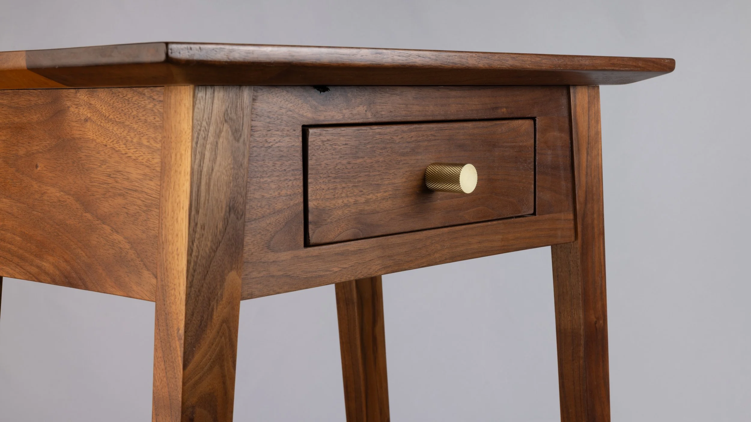 Close-up of a wooden side table with a single drawer and a brass-colored knob.