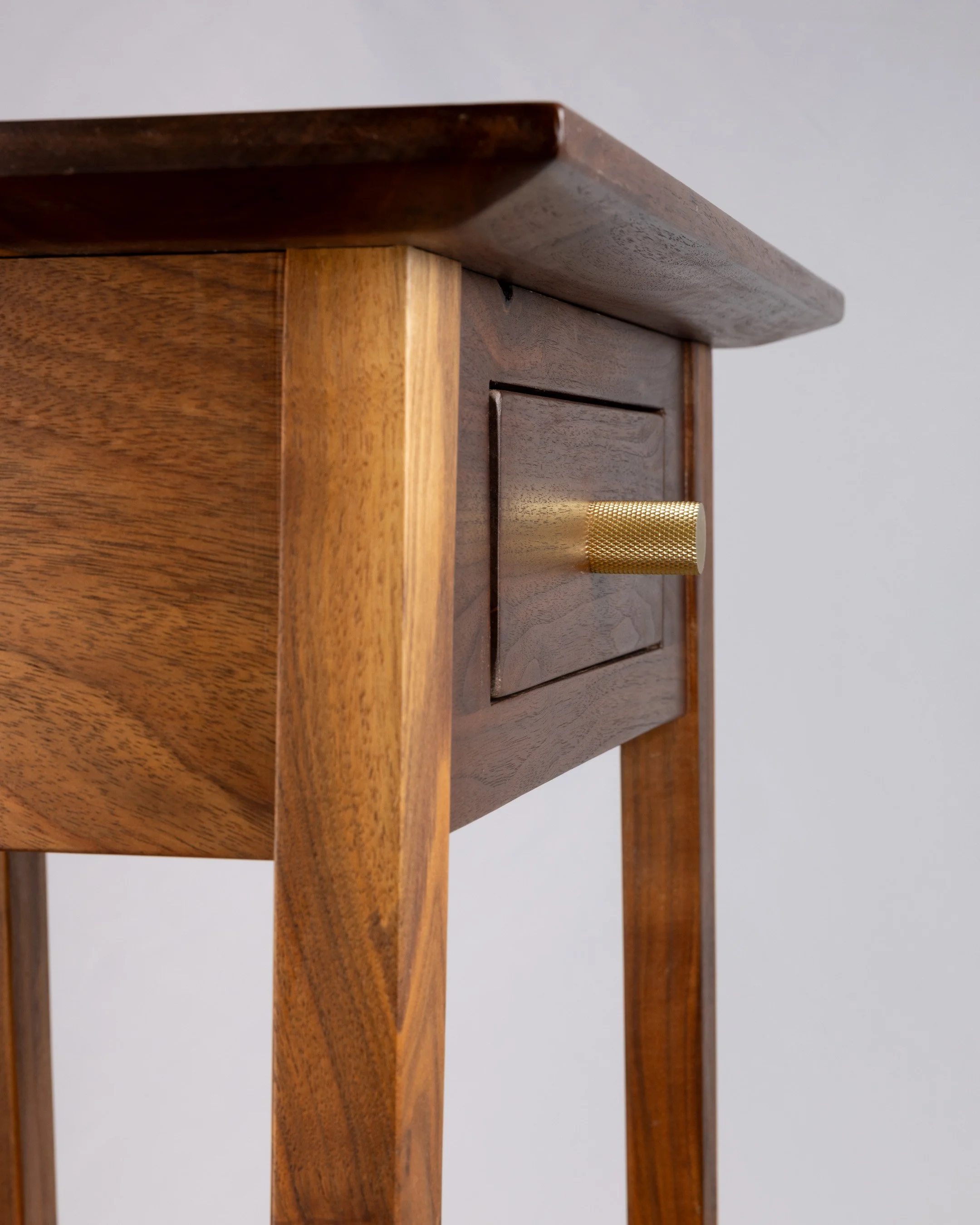 Close-up of a wooden side table with a drawer, featuring a gold textured knob.
