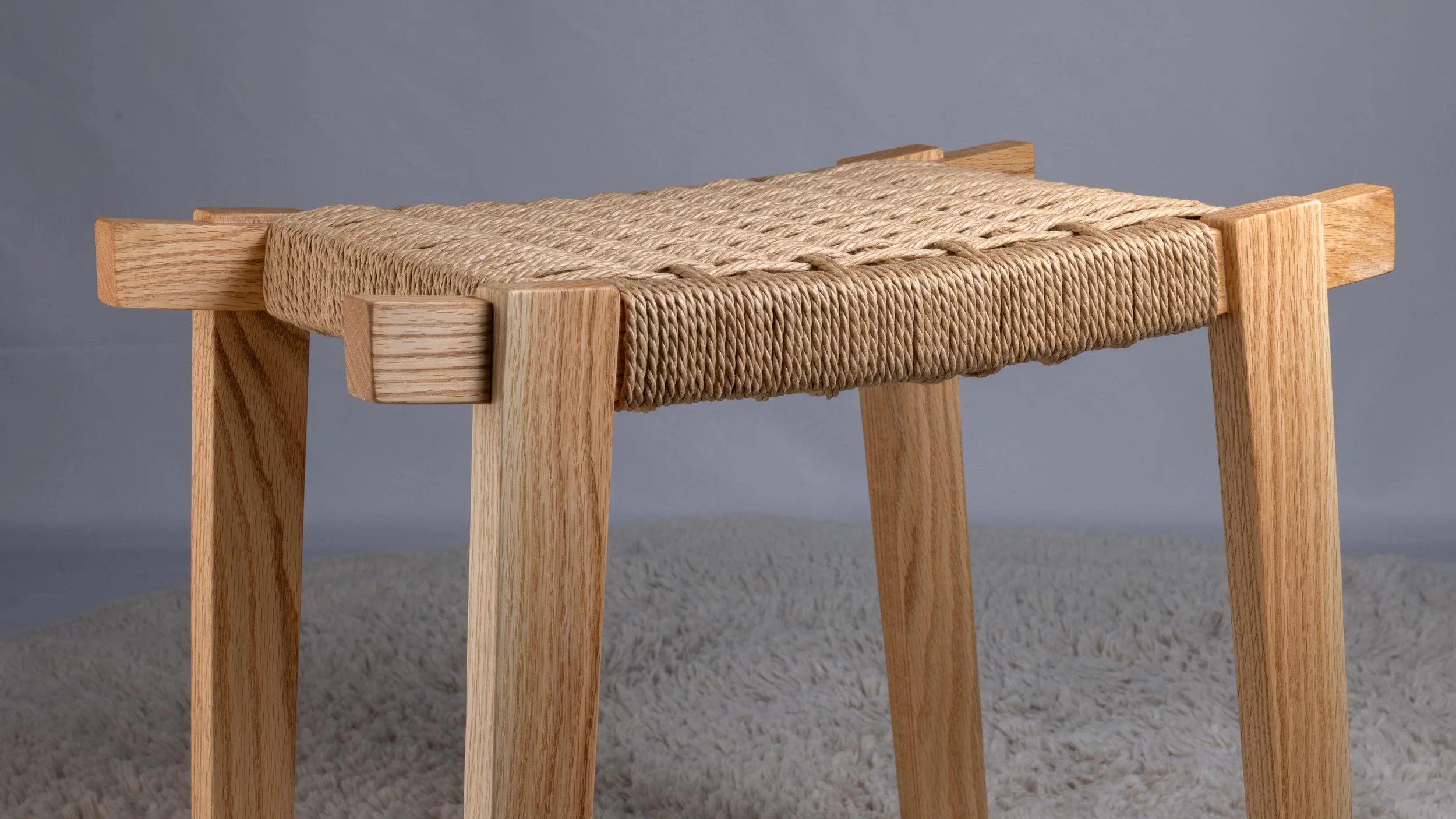 A wooden stool with a woven natural fiber seat.
