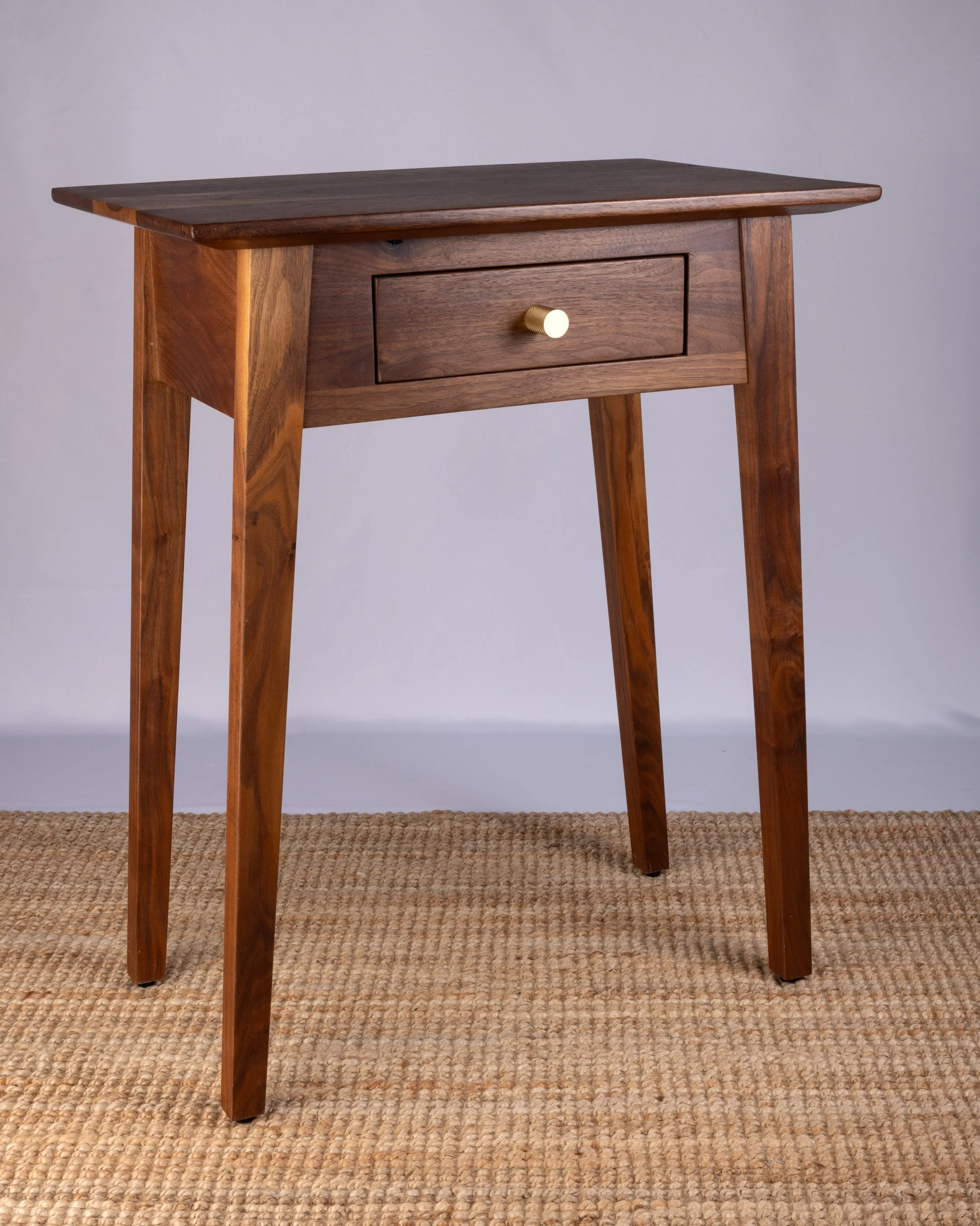 A wooden side table with a drawer and a brass round knob.