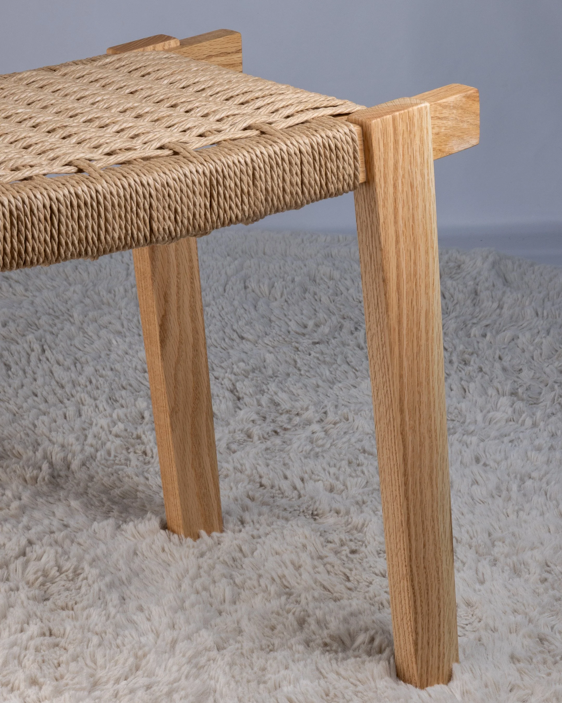 Close-up of a wooden stool with a woven rope seat.