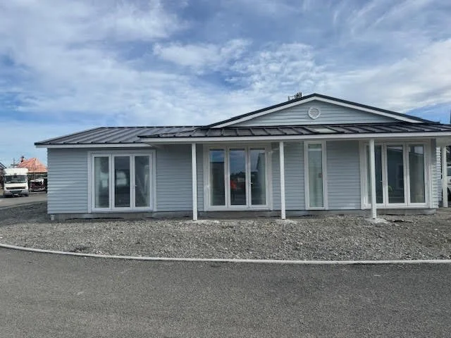 Single-story commercial building with sliding glass doors, white siding, a metal roof, and a gravel parking area in front.