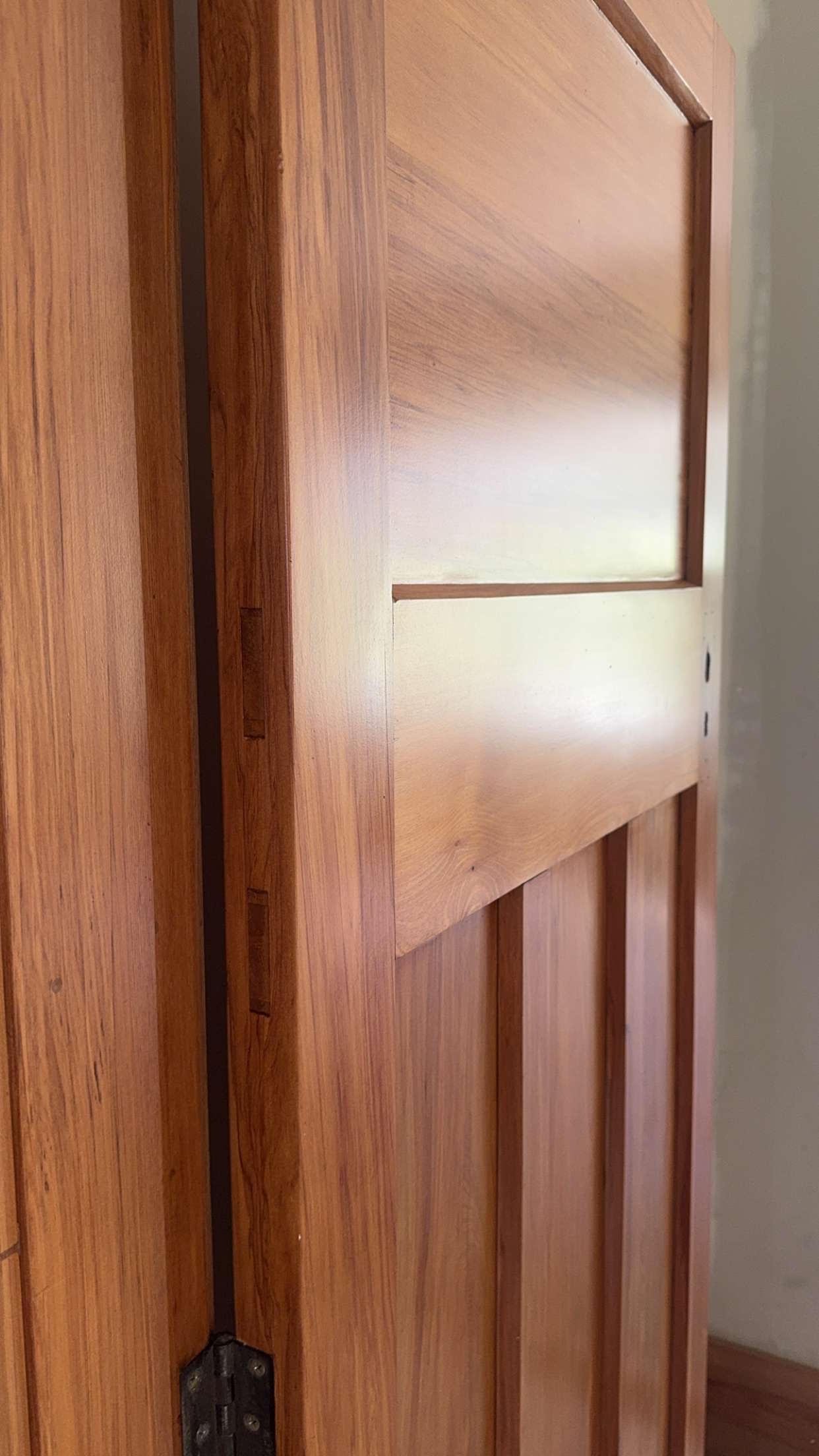 Close-up of a wooden door with decorative paneling, partially open revealing the door's hinge.