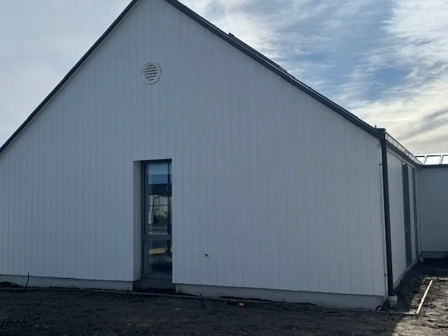 A white building with a sloped roof and a small window and door, set against a partly cloudy sky.