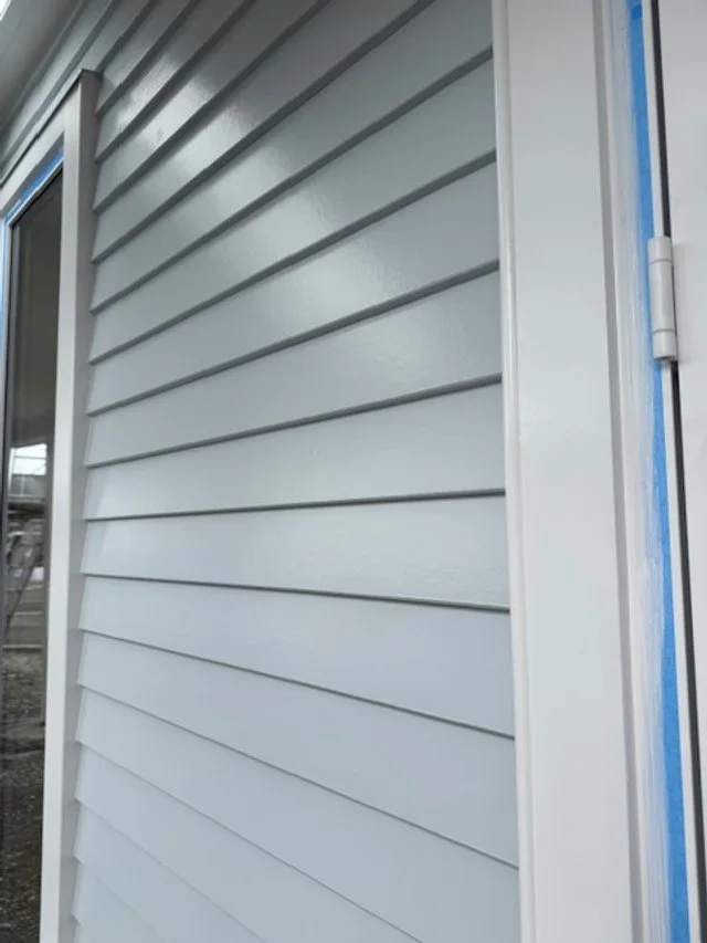 Close-up of gray vinyl siding on an exterior wall of a building, with part of a window and trim visible.