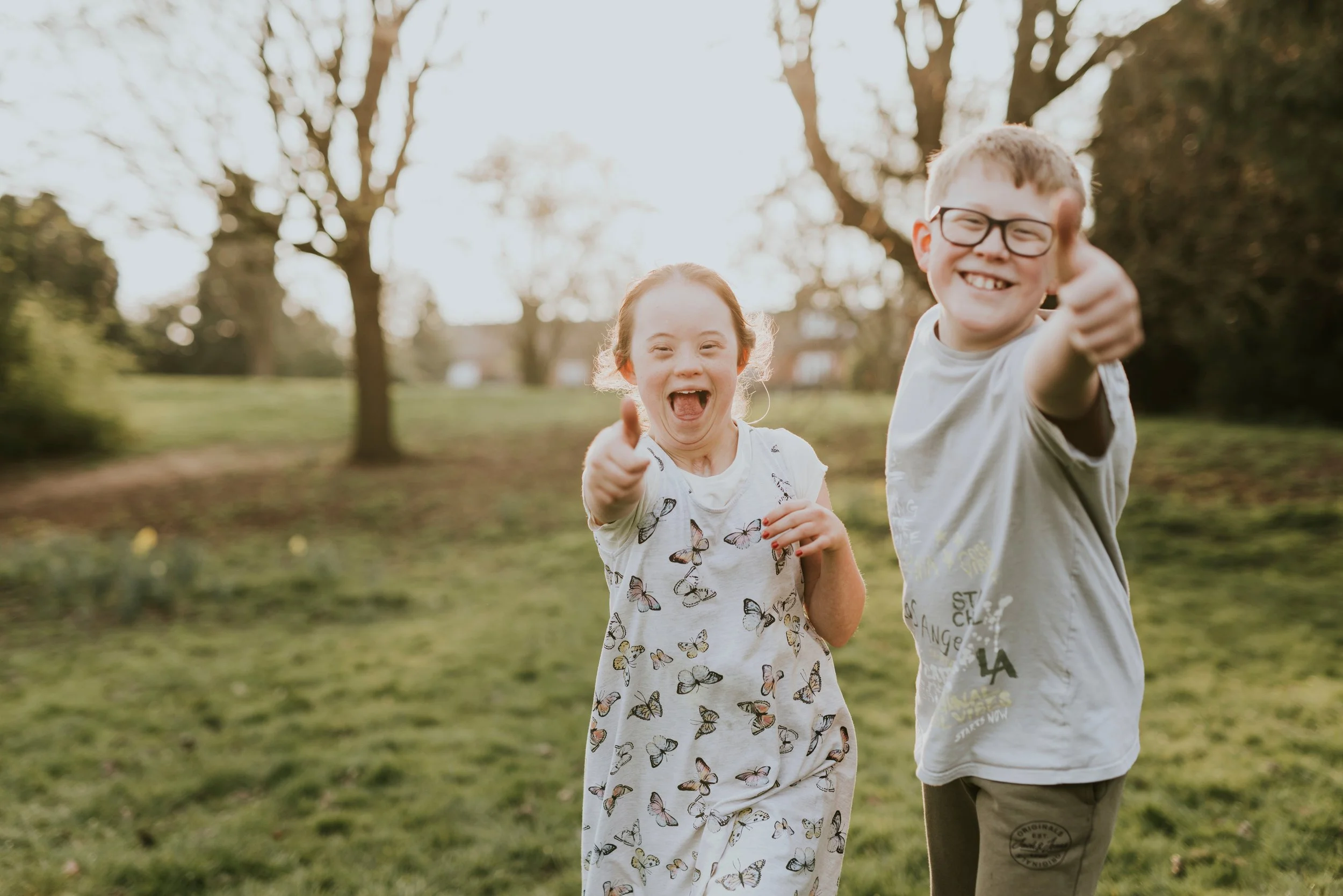 Siblings in a field having fun posing for the camera with thumbs up