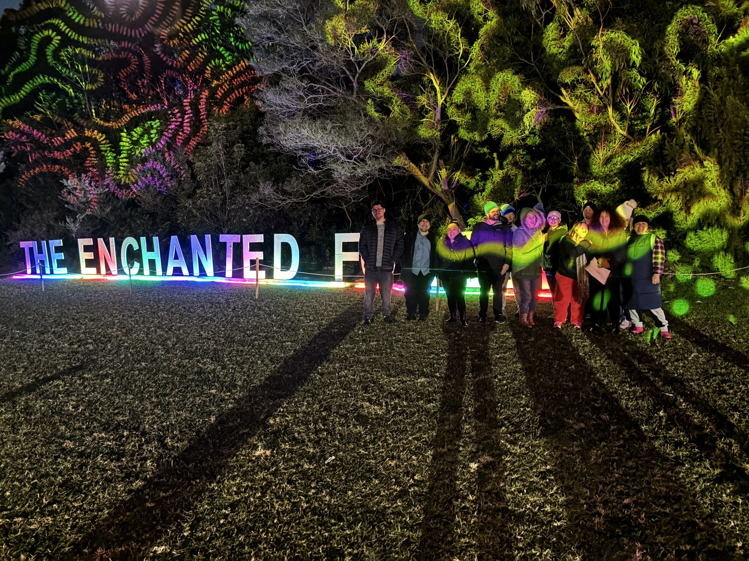 A group of participants standing next to the Enchanted Forest sign lit up at night