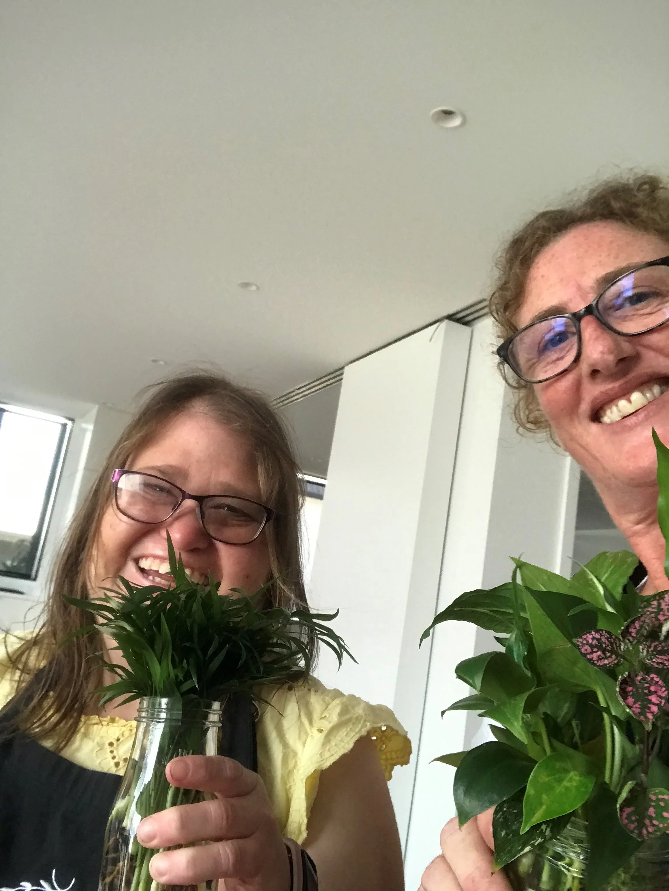 A participant and support worker smiling, holding plants 