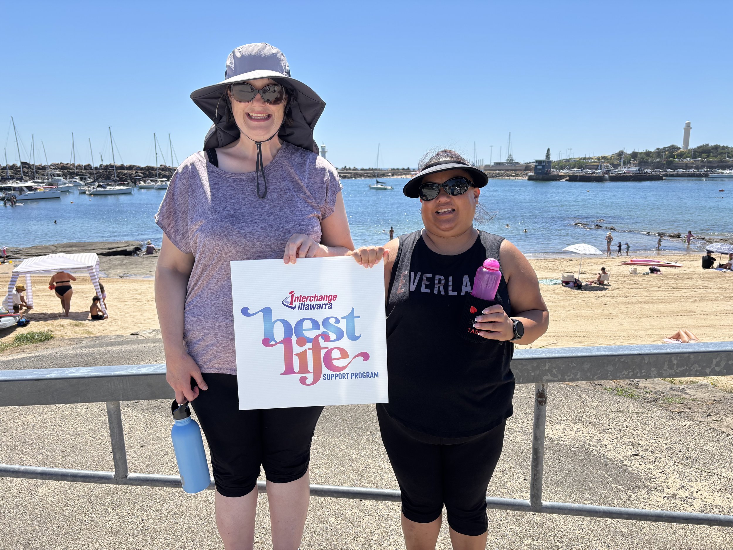 Two women holding up a BestLife sign at Wollongong harbour