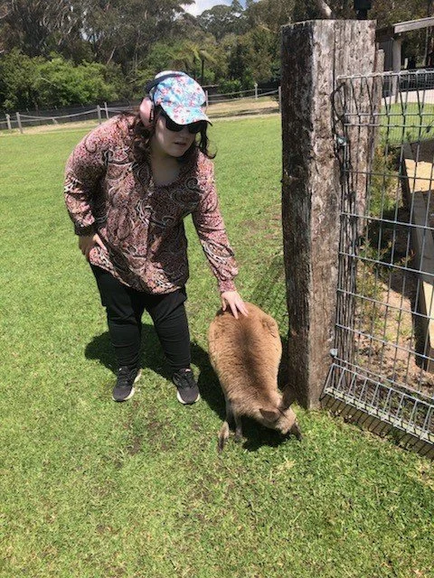 A participant with headphones on patting a wallaby on the grass