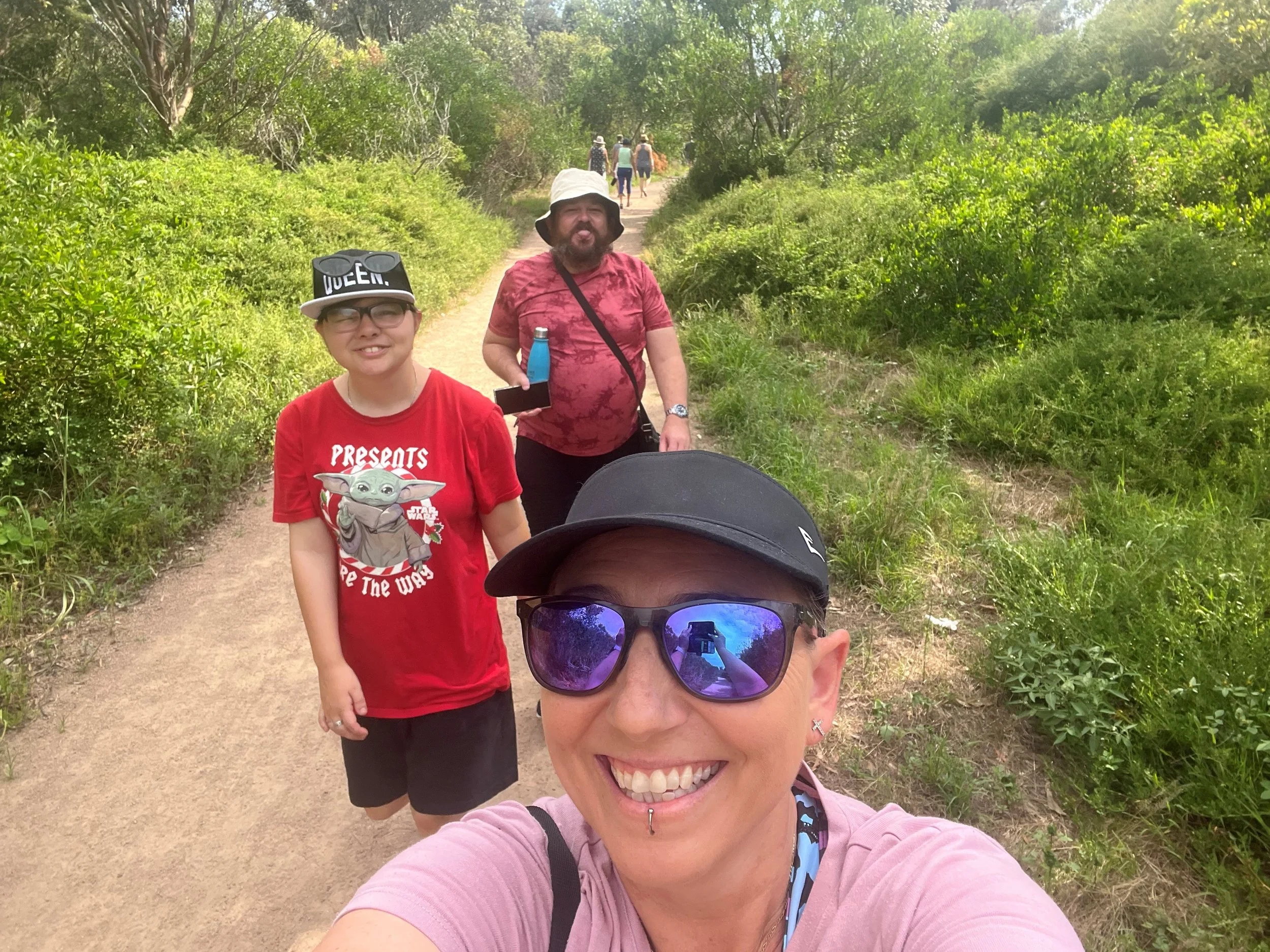 A woman taking a selfie on a bushwalk with two participants in the background