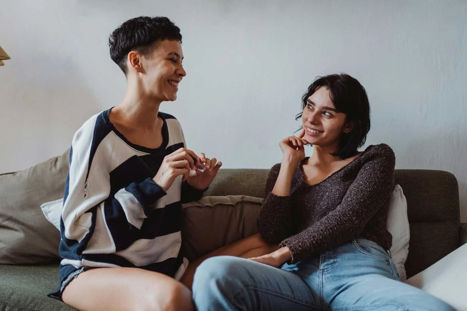 Two women sitting on a couch, smiling and engaging in conversation indoors.
