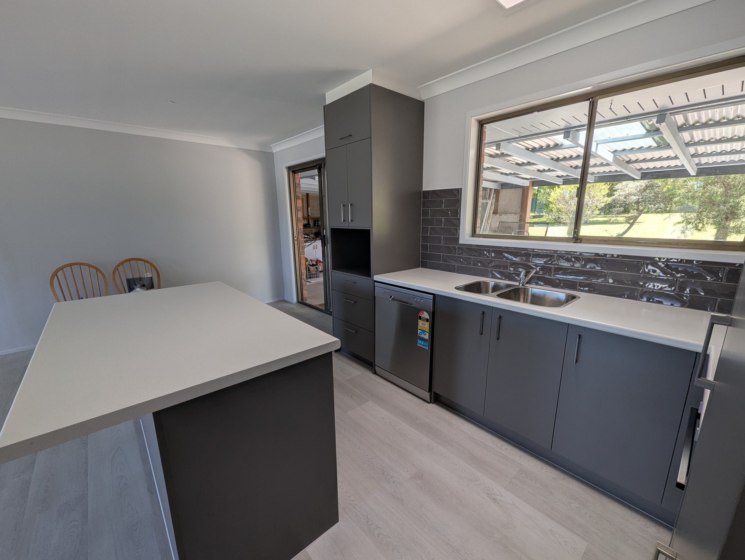 Modern kitchen with gray cabinets, white countertops, a double sink, a window overlooking a grassy yard, and a small island with a white countertop.