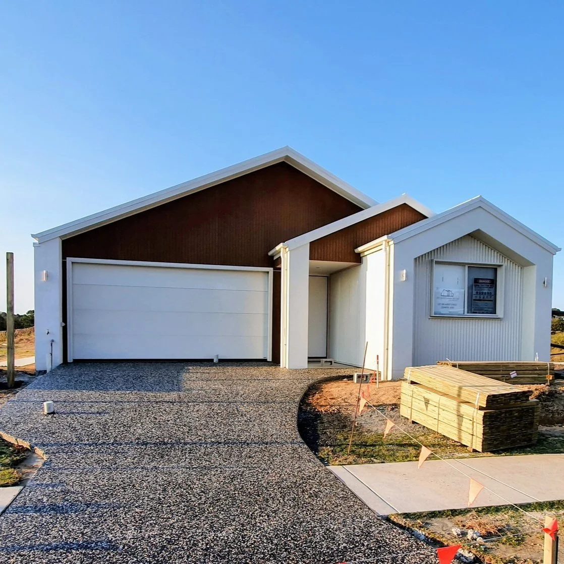 Newly constructed modern house with a textured driveway, brown and white exterior, and construction materials nearby.