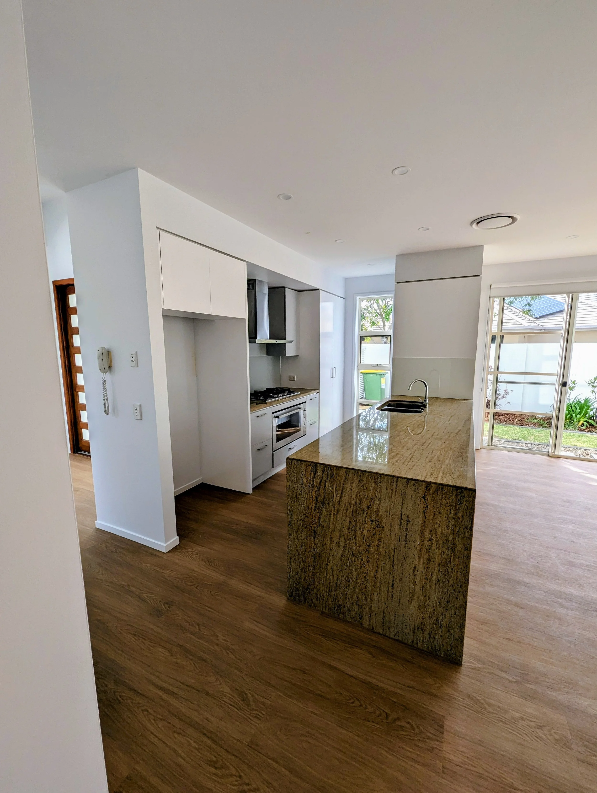Modern kitchen with granite island, white cabinets, wood flooring, and large windows overlooking a garden.