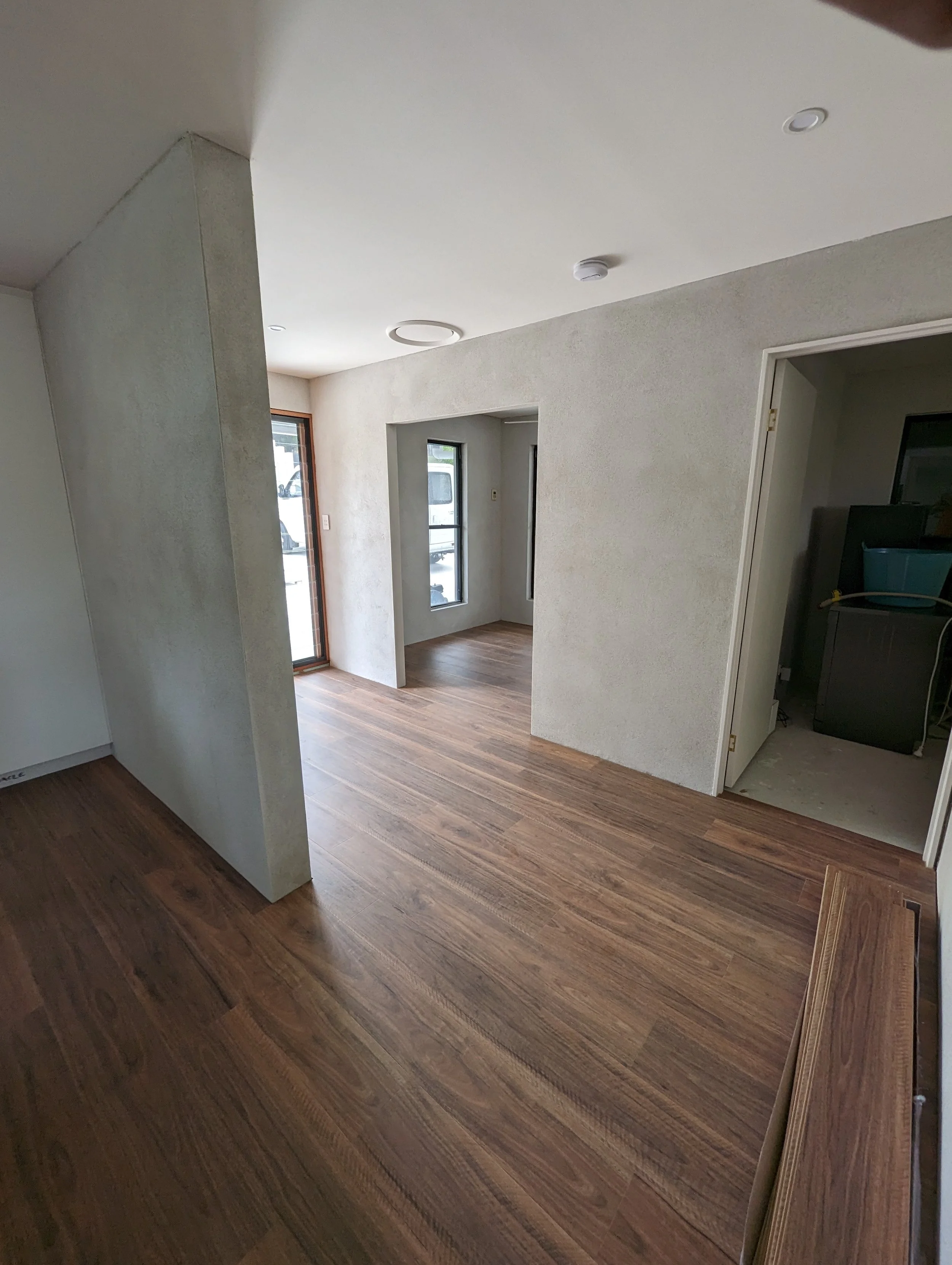 Room with wooden floors, white textured walls, with a doorway and windows.