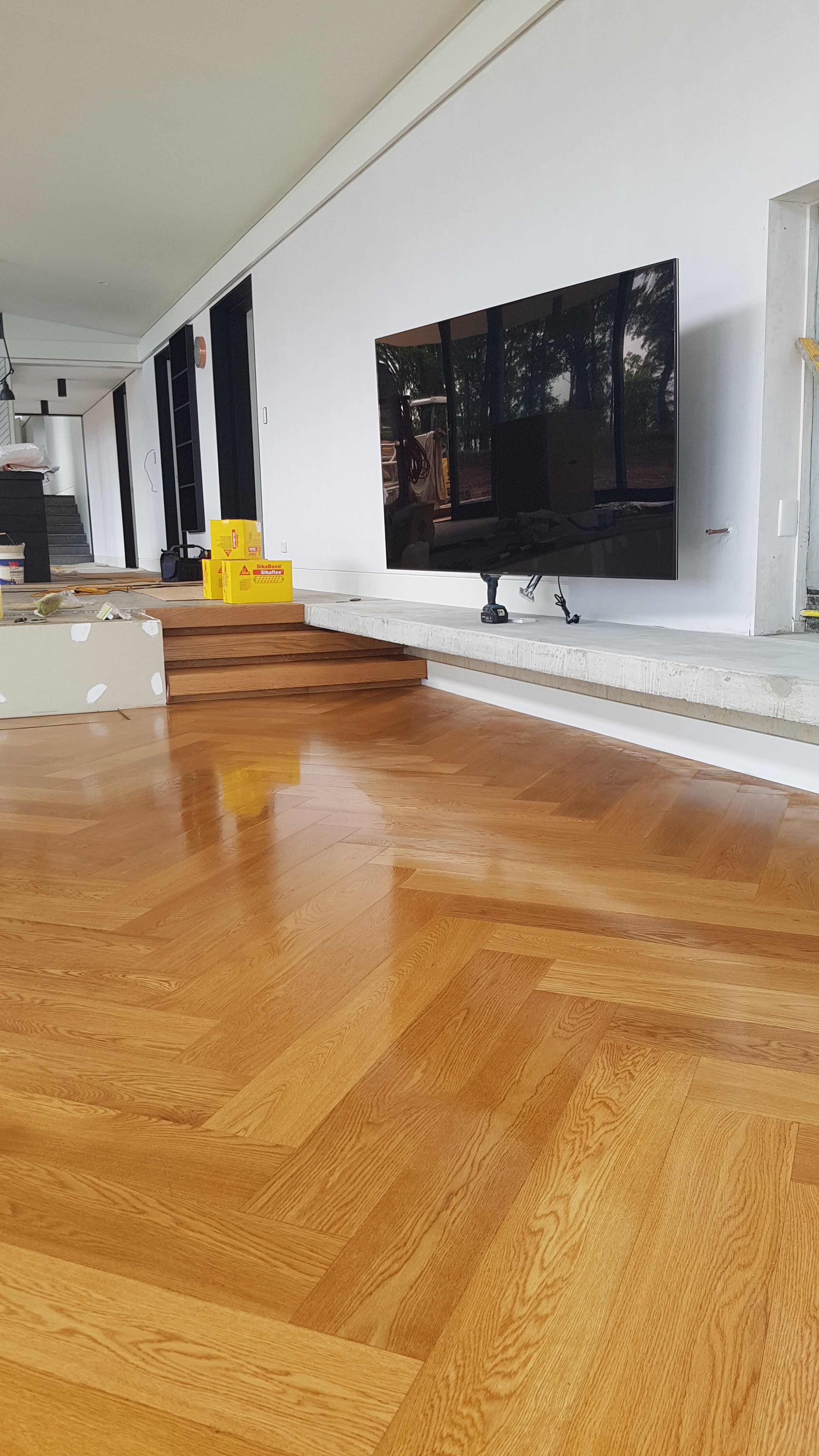 A room with newly installed wooden flooring, a wall-mounted TV, and construction supplies on the left side.