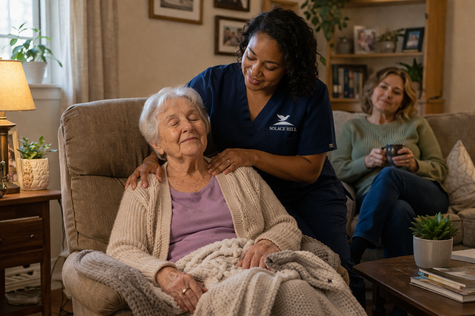 A young woman showing affection with a warm smile and hands on an elderly woman's shoulders as they sit together on a beige sofa in a cozy living room.