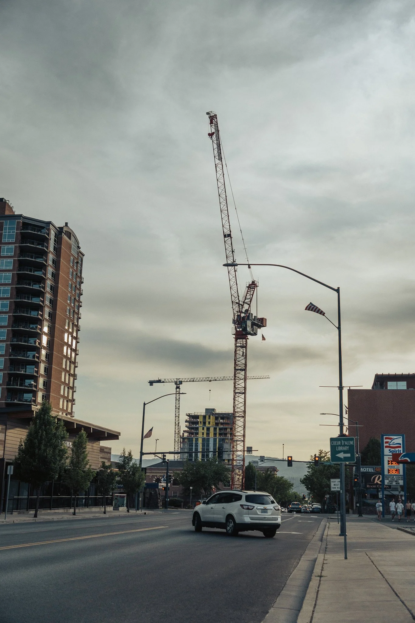City street with construction cranes and high-rise buildings under a cloudy sky.