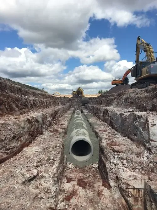 Large concrete pipe positioned in a deep trench during underground pipeline installation on a civil construction site.