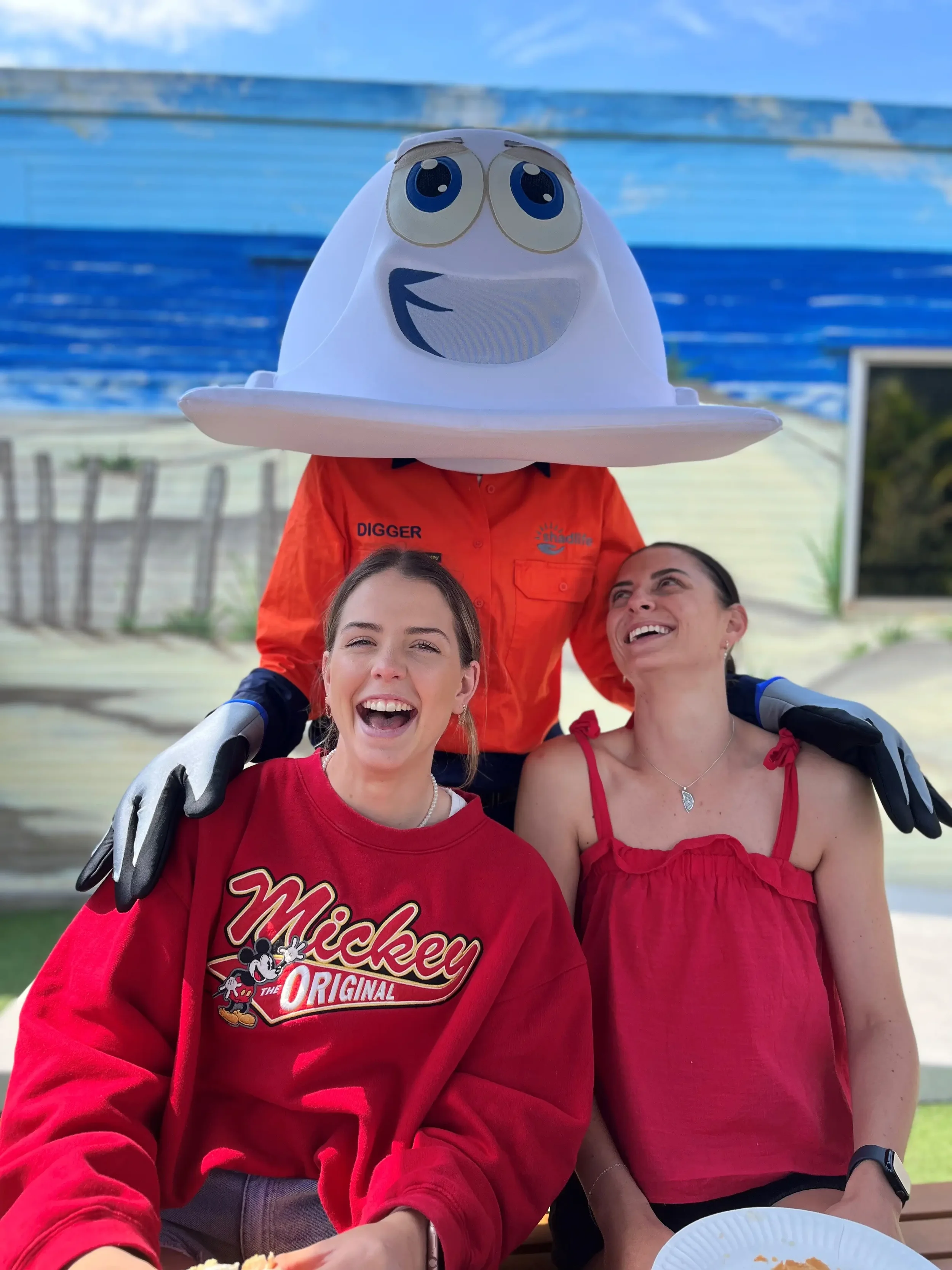 Two girls smiling wearing red tops with a Digger mascot standing behind them.