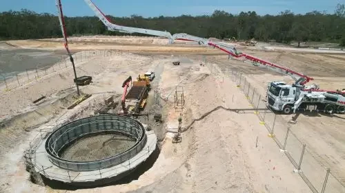 Construction site with concrete machinery, a cement truck, and a concrete pump extending into the site.