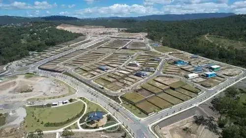 Aerial view of SkyRidge masterplanned community with multiple houses, roads, and a park with a pond, surrounded by green hills and open land.